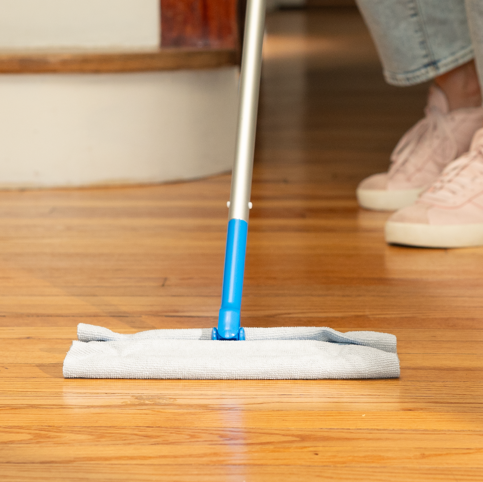 Person cleaning a wooden floor using a dust mop and a microfiber cleaning cloth in place of the disposable mop pad.