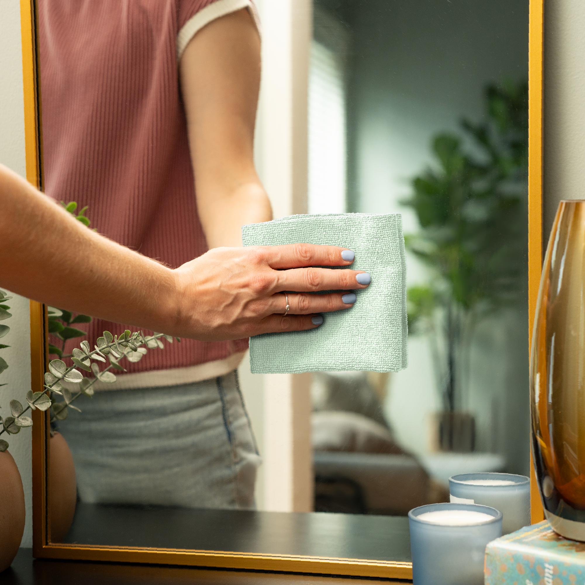 Person cleaning a mirror with a microfiber cleaning cloth in a home setting.