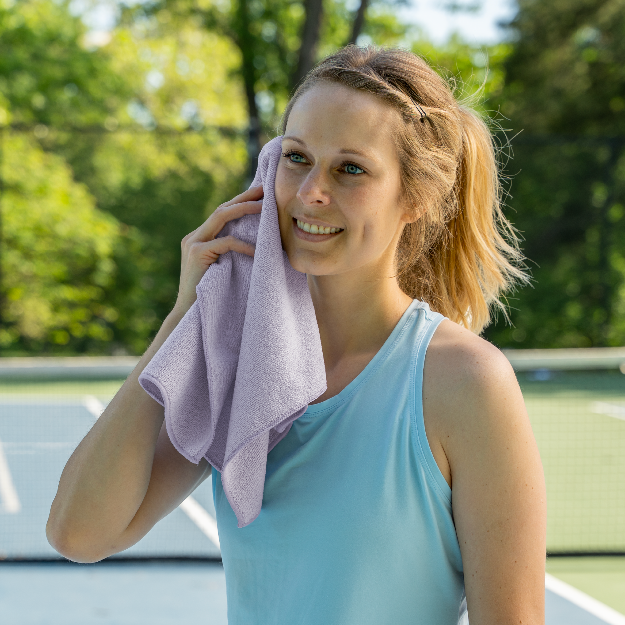 Woman wiping sweat with the absorbent purple terry gym towel on a tennis court