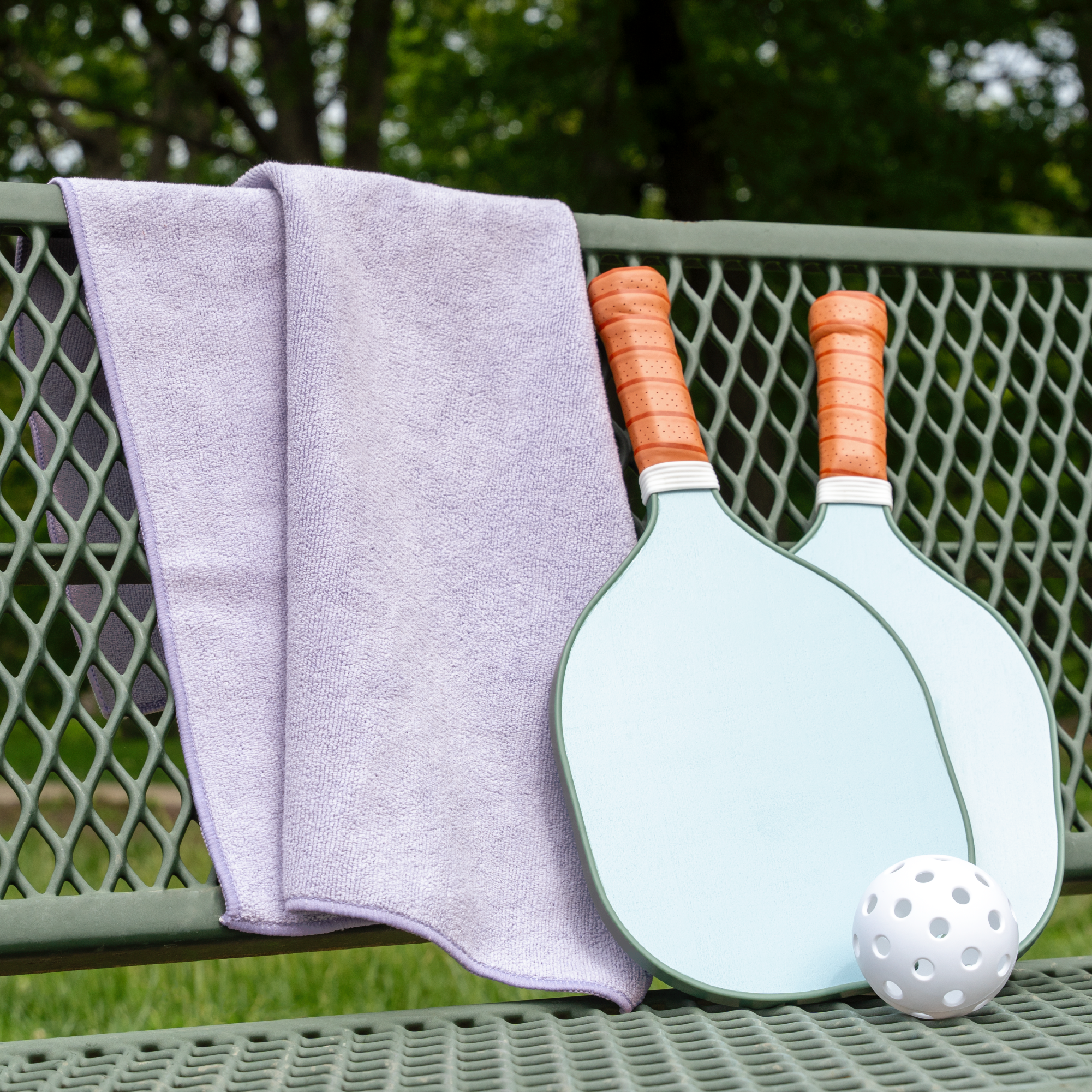 purple gym towel draped on a bench with 2 pickleball paddles