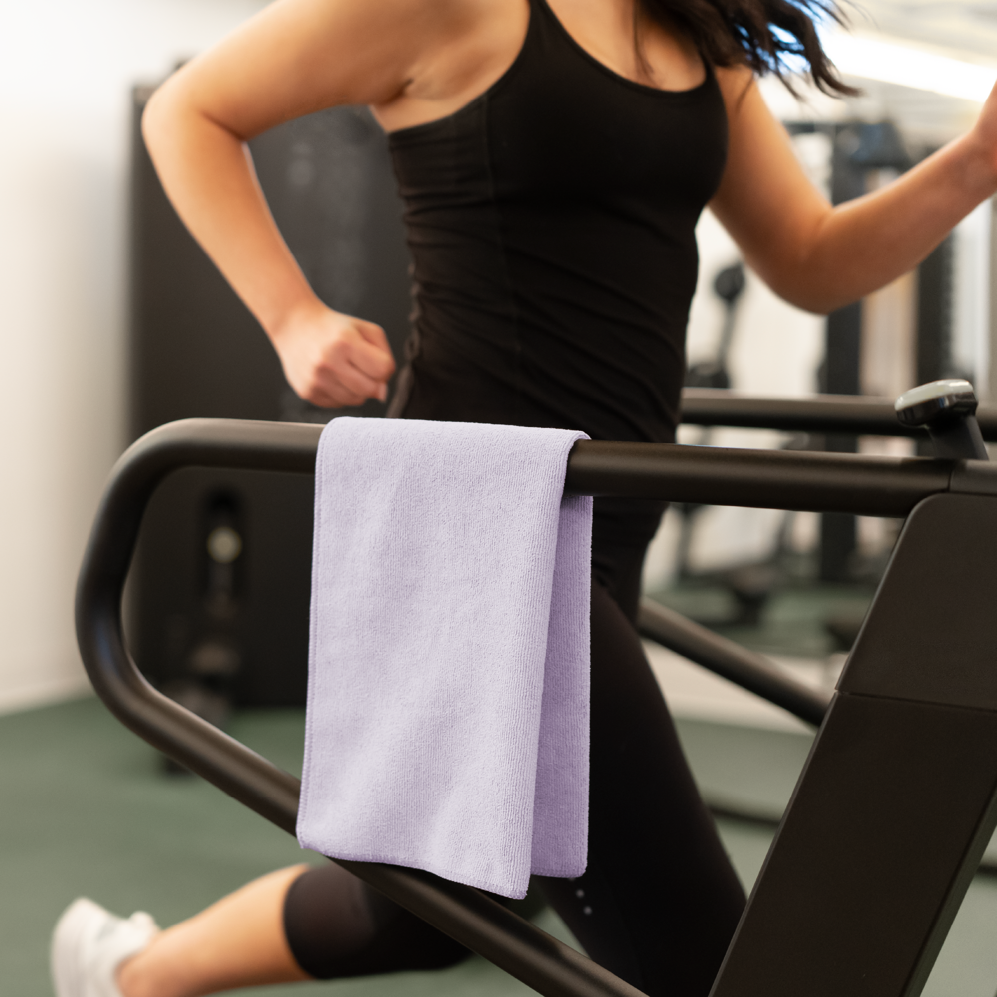 Person using a treadmill with a purple gym towel draped over the handlebars in a gym setting