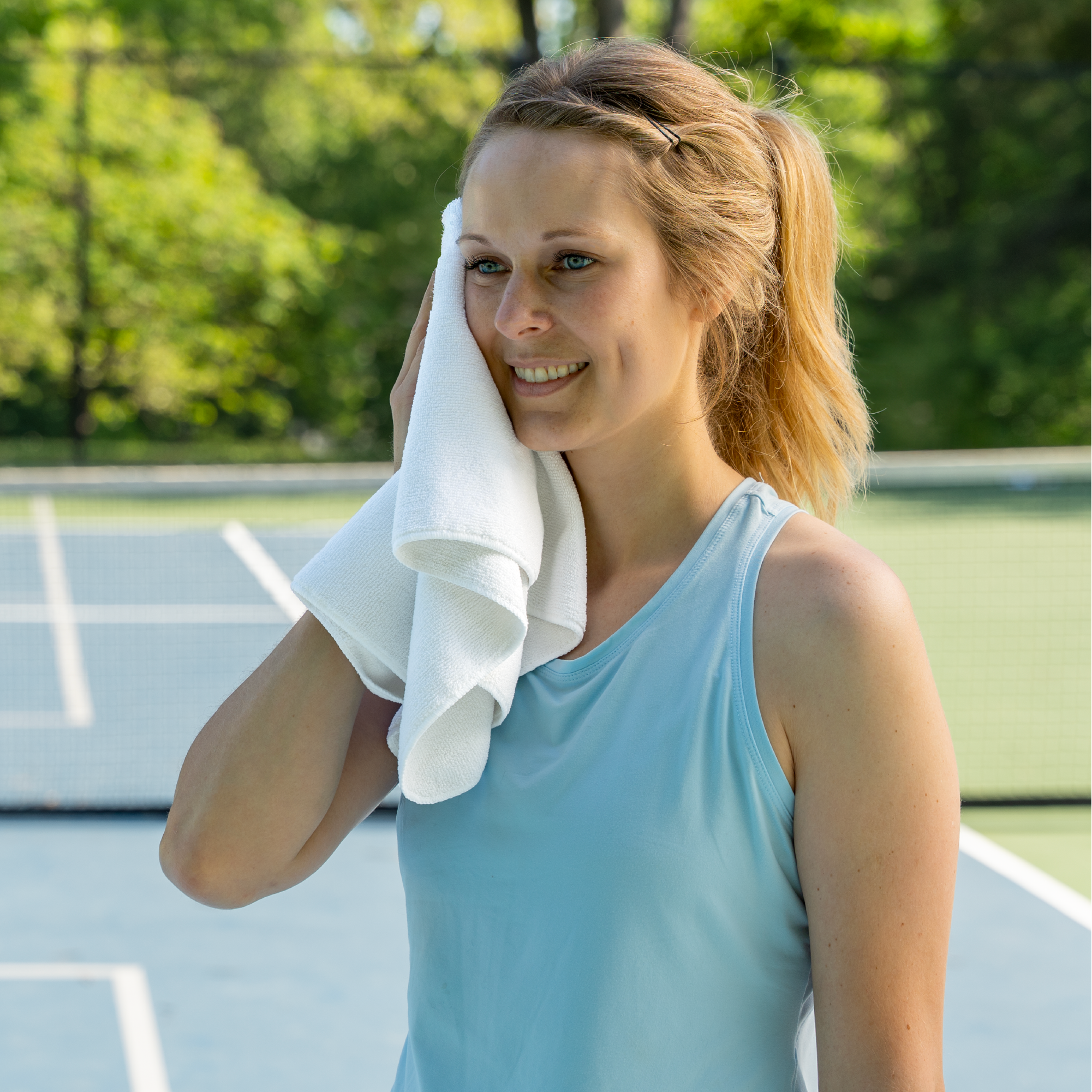 Woman with a super absorbent gym towel towel on a tennis court wiping sweat from forehead