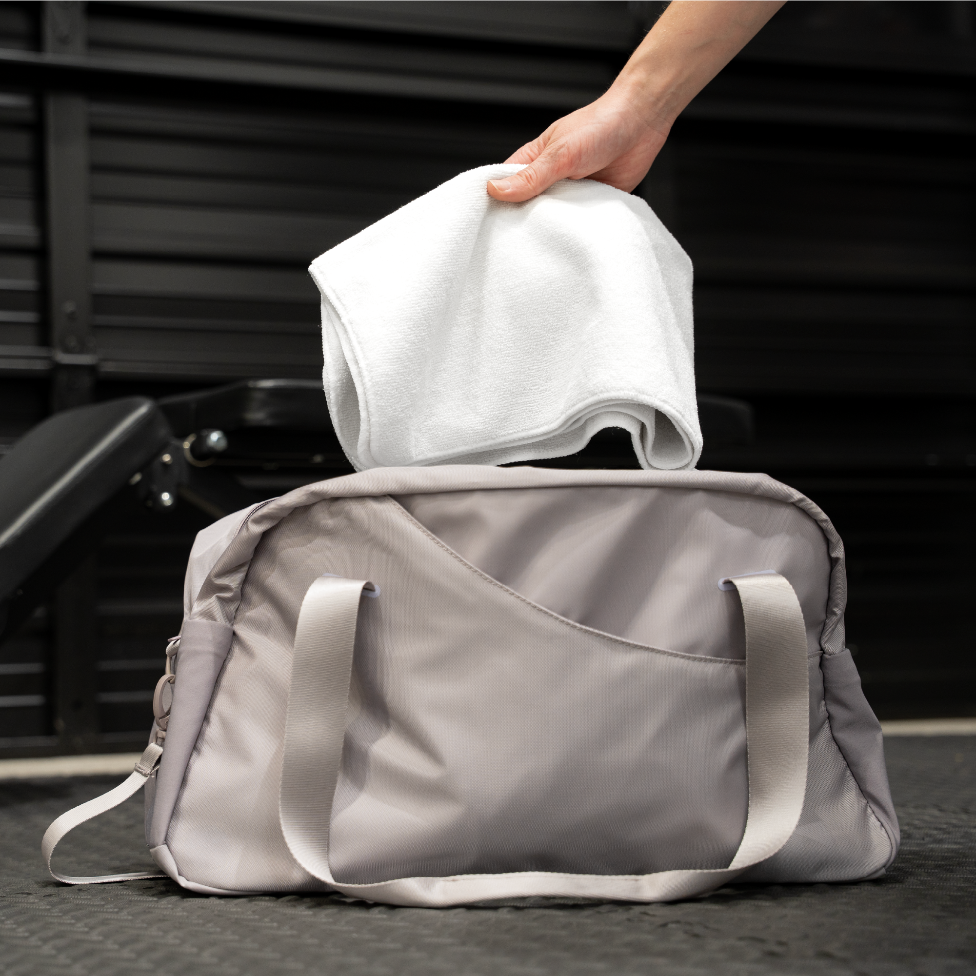person placing a folded, compact exercise towel into a duffle bag for on-the-go activities