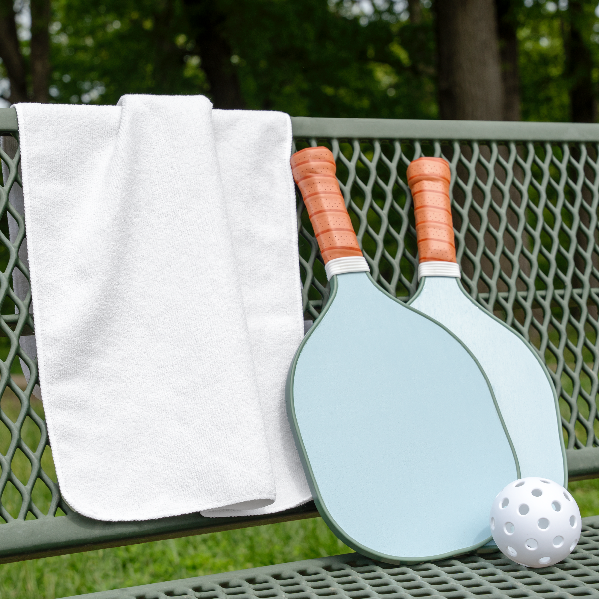 microfiber terry exercise towel draped over a park bench next to 2 pickleball paddles