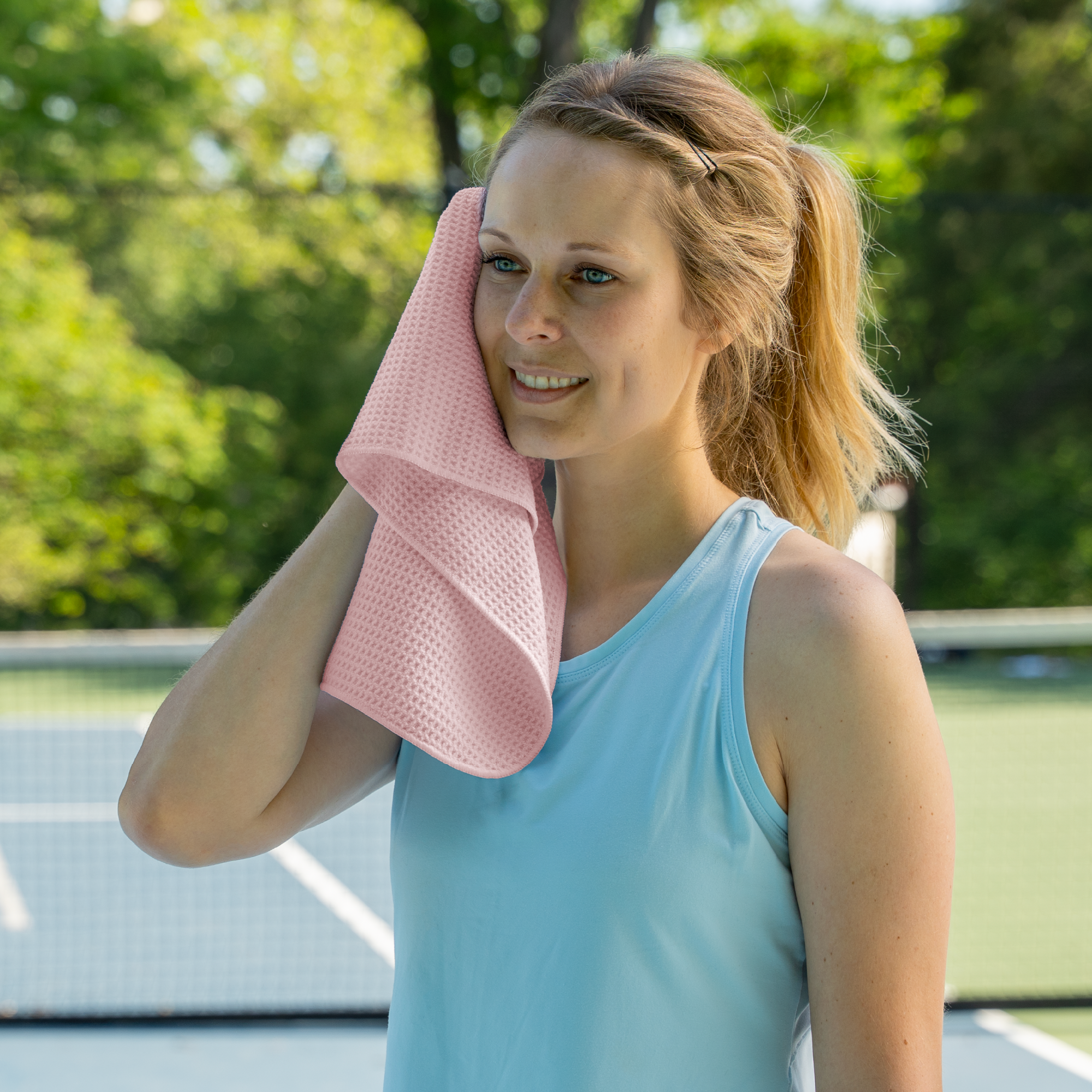 Woman wiping sweat with a pink honeycomb gym towel on a tennis court