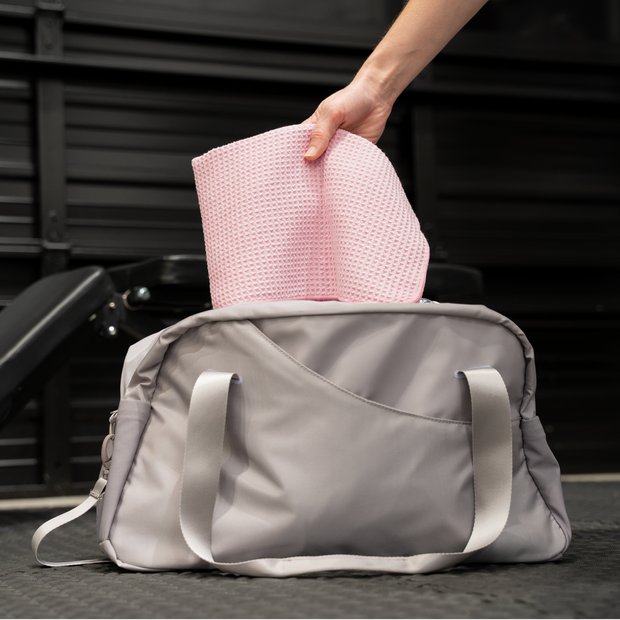 Person placing a pink honeycomb gym towel into a duffel bag for on-the-go