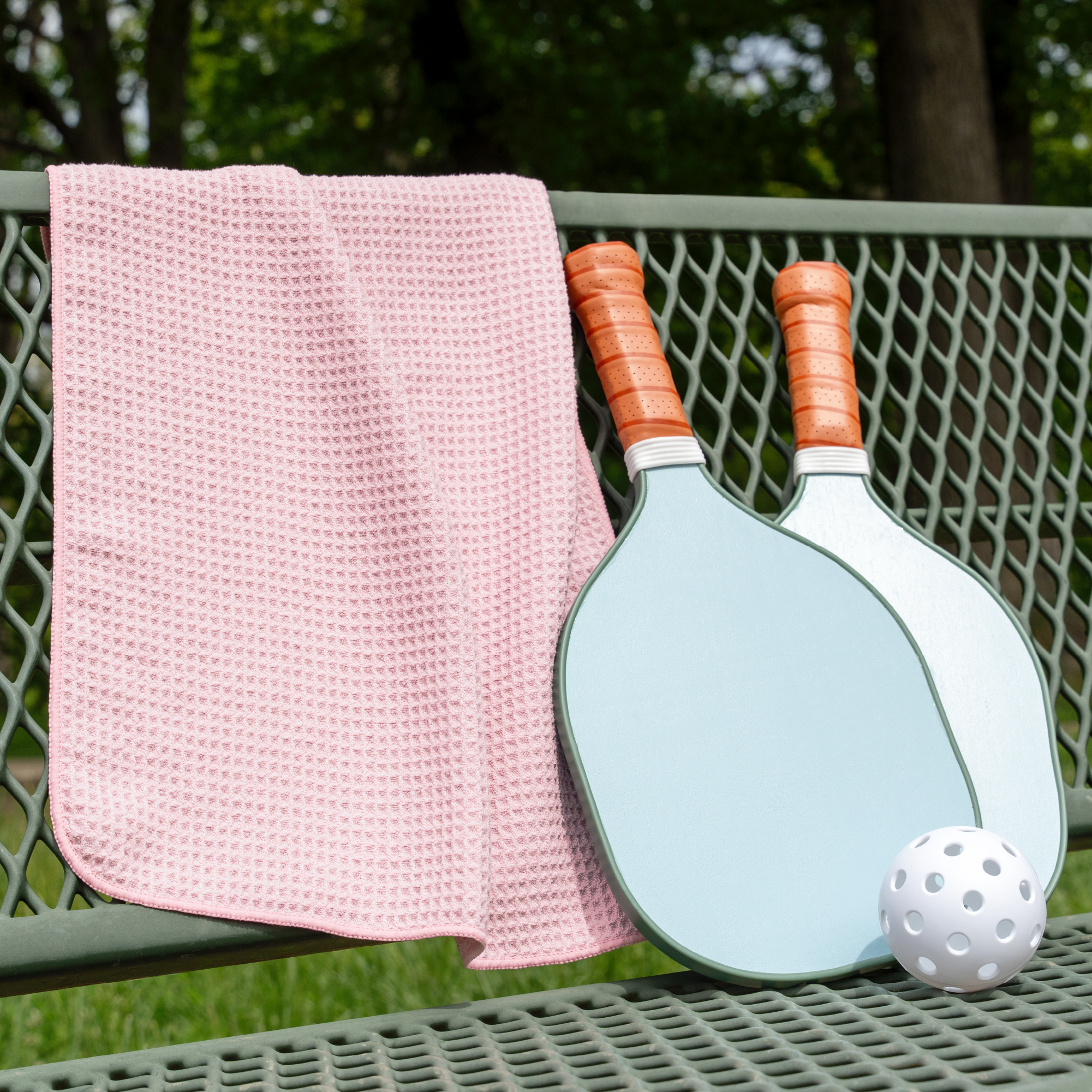 Pink gym towel draped over a bench with 2 pickleball paddles