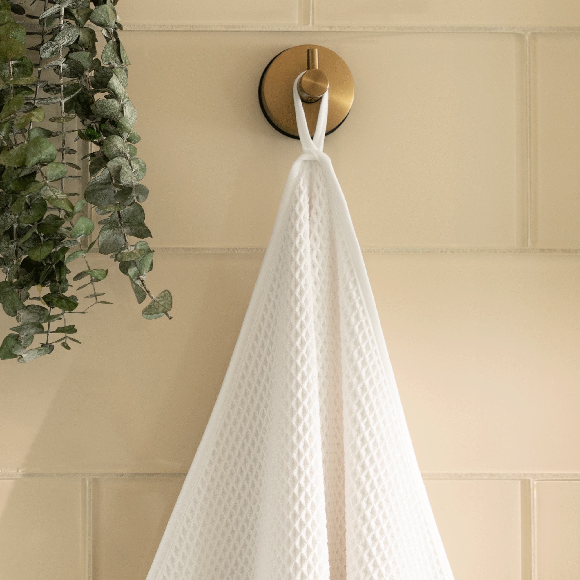 white waffle bath towel hanging on a gold hook against a tiled shower wall