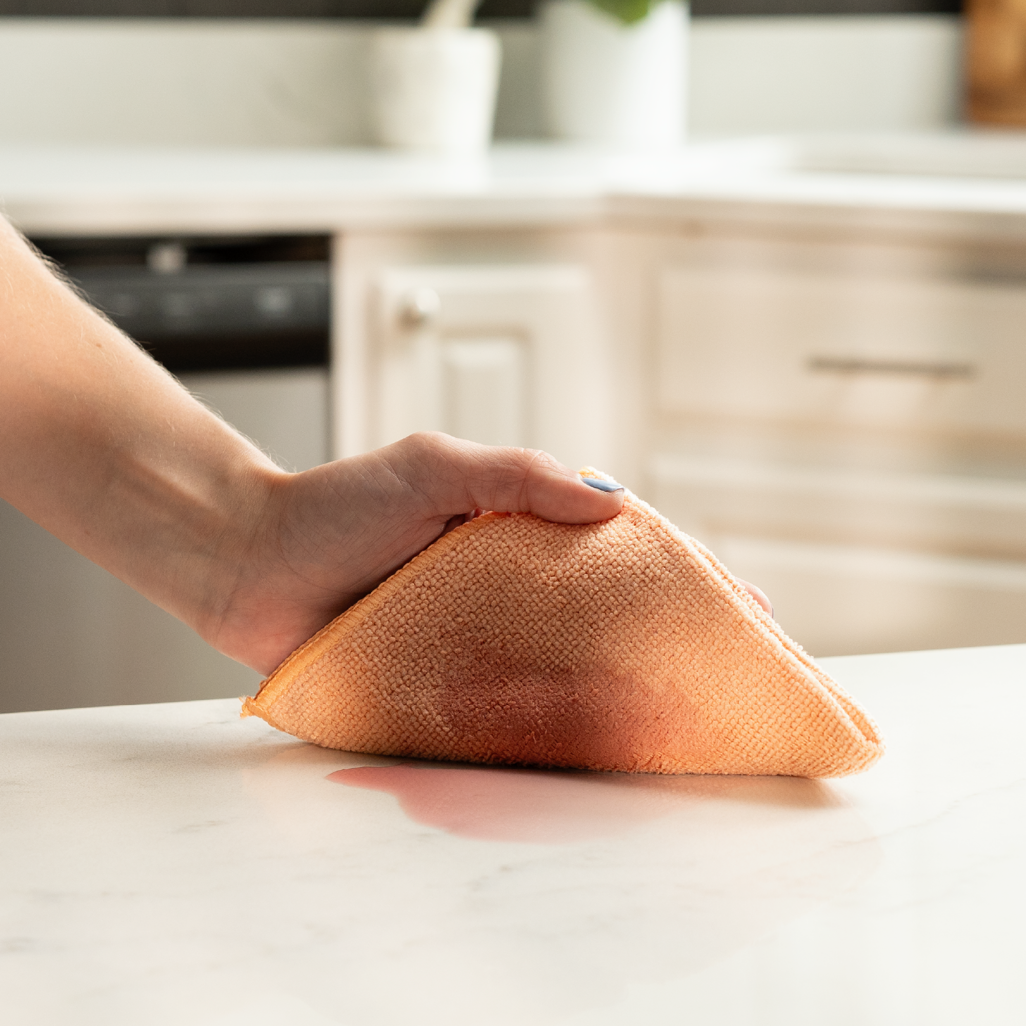 Coral microfiber cleaning cloth wiping up a spill with ease on a kitchen counter