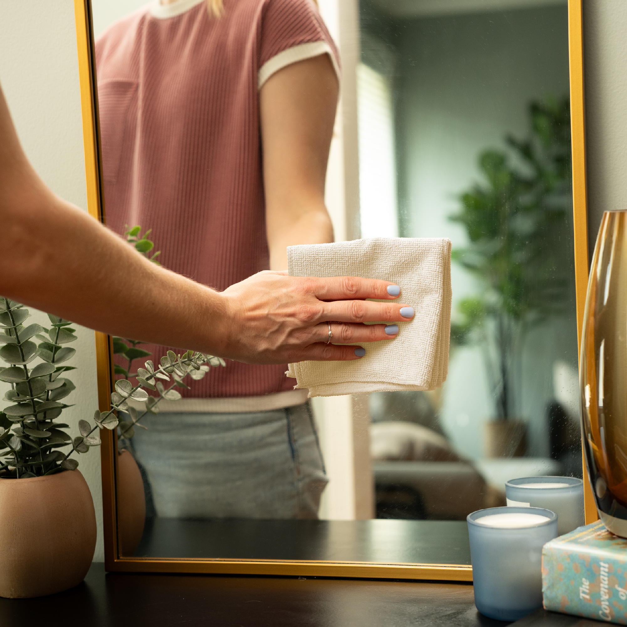 Person cleaning a mirror with a cream cloth in a home setting.