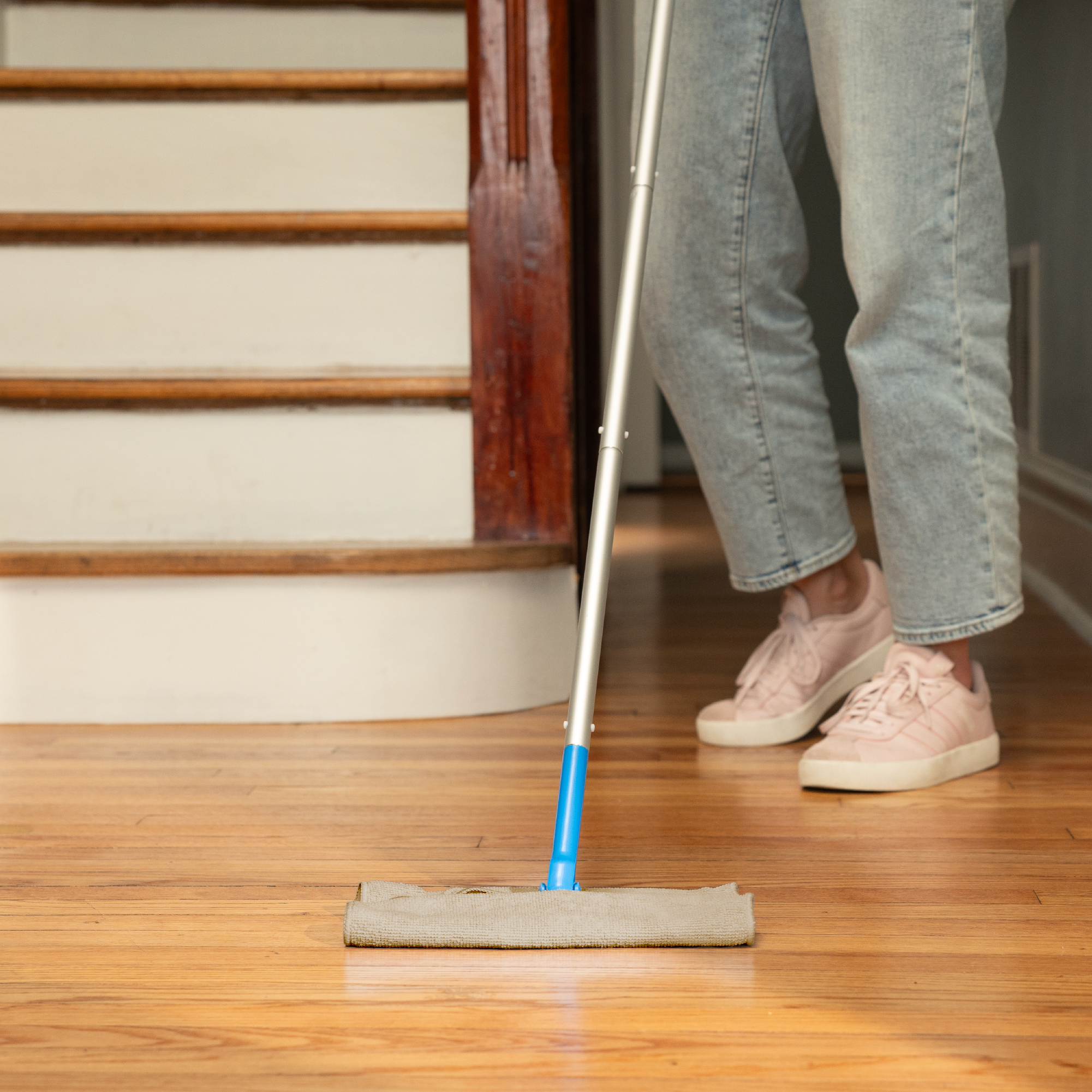 Person cleaning a wooden floor using a dust mop and a microfiber cleaning cloth in place of the disposable mop pad.