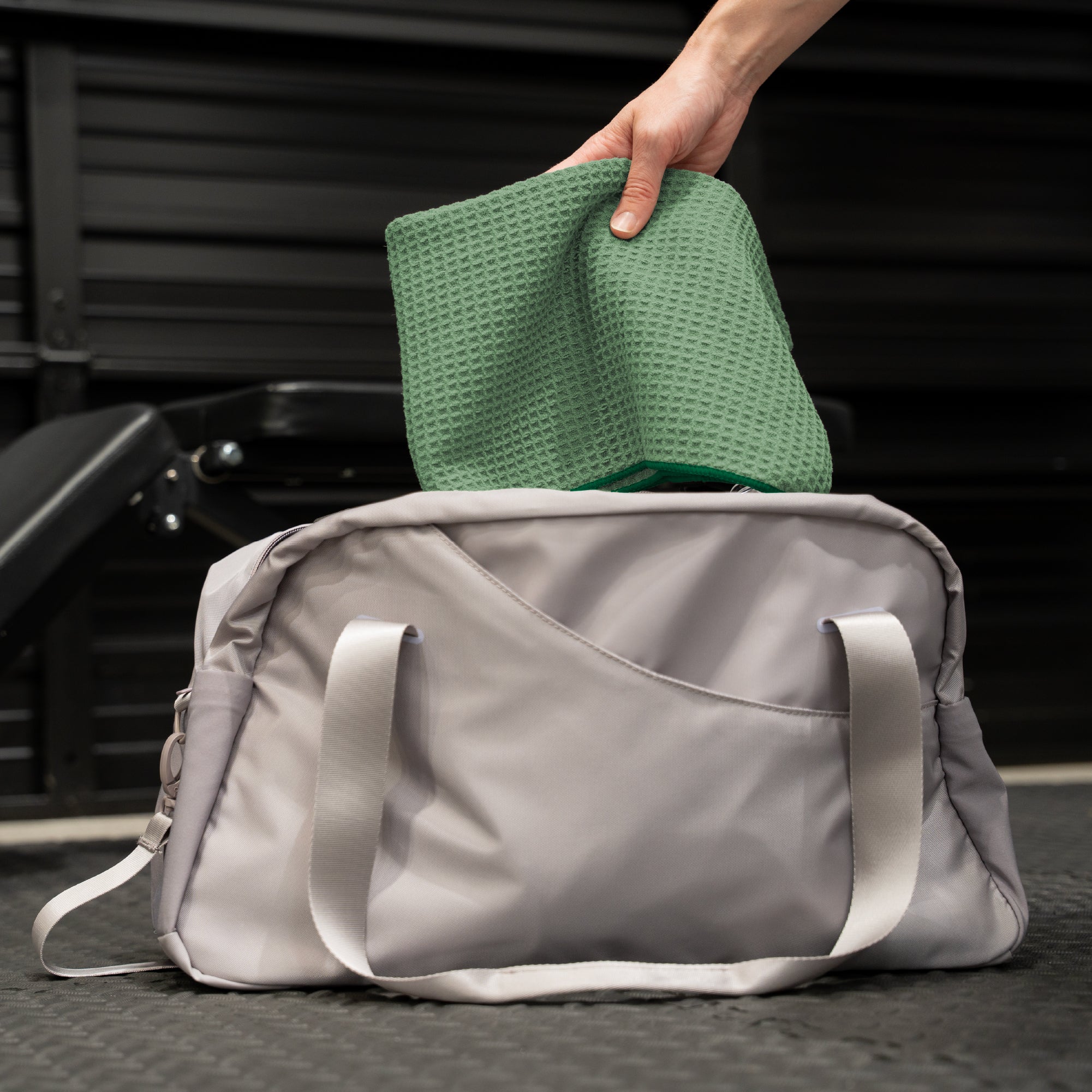 Person placing a green gym towel into a duffel bag for on-the-go