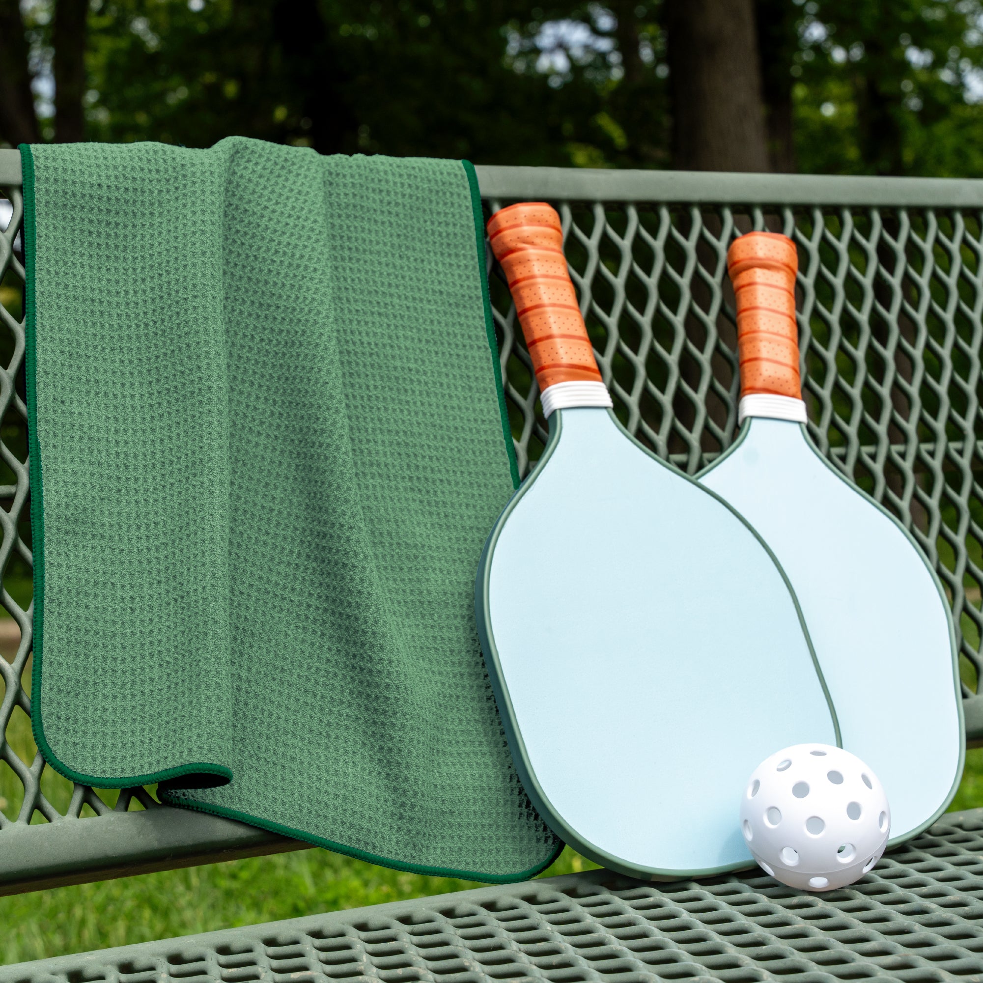 Green honeycomb gym towel draped on a bench with 2 pickleball paddles