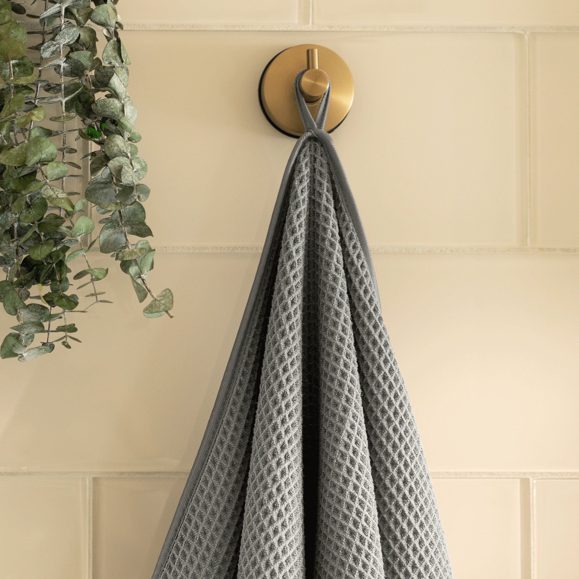 grey waffle bath towel hanging on a gold hook against a tiled shower wall
