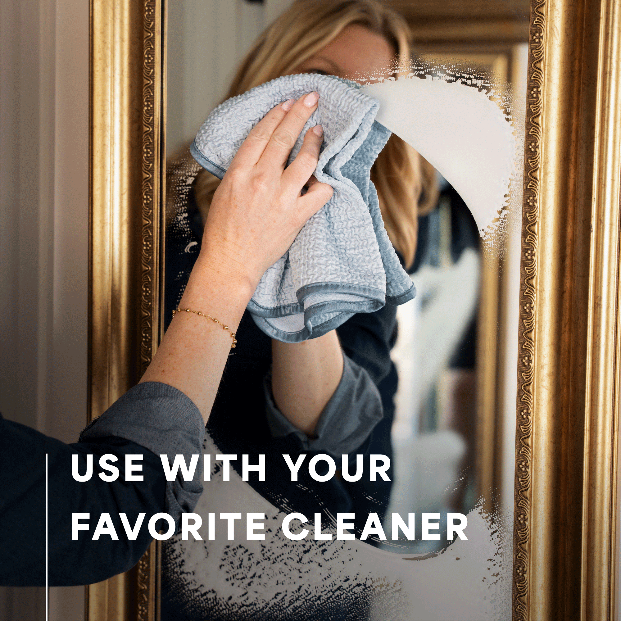 A person wipes a large ornate gold-framed mirror with a light blue cloth. The text overlay reads 'USE WITH YOUR FAVORITE CLEANER'.